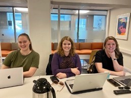Tre stipendiater sitter ved et bord og smiler til kamera