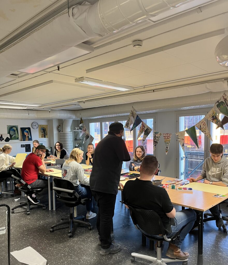 Folk jobber med akvarellmaling rundt et bord i et klasserom.